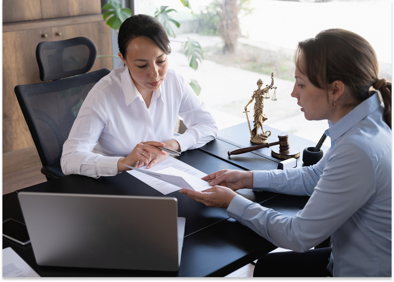 Two women discussing legal documents at desk.